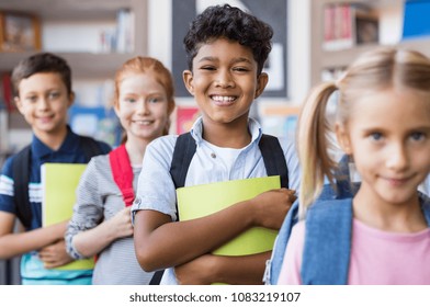 Portrait of a happy multiethnic children holding books and wearing backpack at primary school. Schoolboys and cute girls in a row holding notebook and looking at camera. Elementary child smiling.
