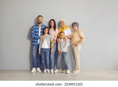 Portrait of a happy multigenerational family. Cheerful, joyful, smiling mother, father, grandfather, grandmother and little children standing all together by a light grey wall in the studio - Powered by Shutterstock