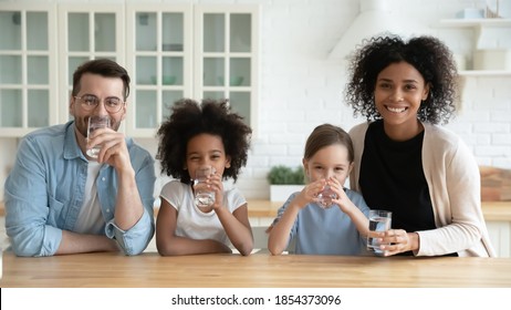 Portrait Happy Multiracial Family Drinking Pure Mineral Water In Kitchen, Smiling African American Mother And Caucasian Father With Two Little Daughters Enjoying Fresh Aqua, Healthy Lifestyle Concept