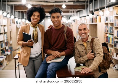 Portrait Of Happy Multiracial Students And Their Female Professor At University Library Looking At Camera.