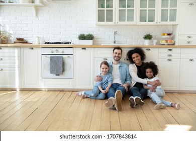 Portrait of happy multiracial young family with little kids sit on warm floor in design modern kitchen, smiling multiethnic parents with small biracial daughters relax in new renovated home together - Shutterstock ID 1707843814