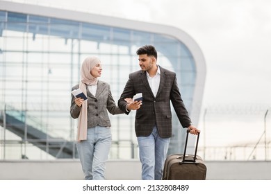 Portrait of happy muslim couple, woman in hijab and manin jacket, walking with passports and tickets outdoors carrying a suitcase and talking each other, going to travel by airplane at modern airport. - Powered by Shutterstock