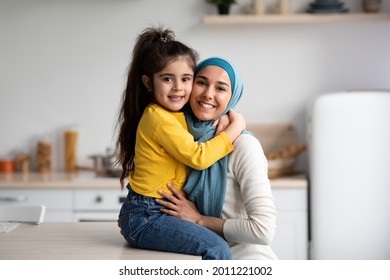 Portrait Of Happy Muslim Mother In Hijab And Little Daughter Posing In Kitchen Interior, Cute Small Girl Hugging Her Islamic Arab Mom And Smiling At Camera, Mommy And Child Having Fun At Home - Shutterstock ID 2011221002