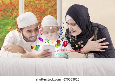 Portrait Of Happy Muslim Parents Teaching Math To Their Child While Lying On The Bed With Autumn Background On The Window