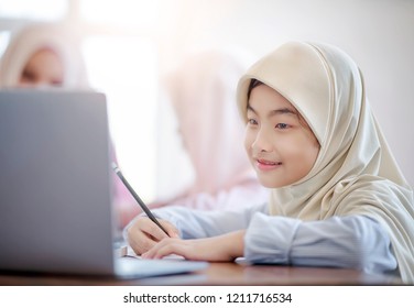 Portrait Of Happy Muslim Student Writing And Using Laptop While Sitting In Classroom With Her Friends.