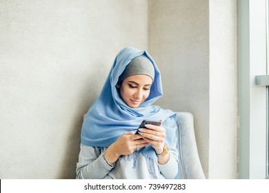 Portrait Of Happy Muslim Woman Using Mobile Phone While Sitting On A Couch