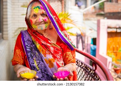 Portrait Of Happy Old Indian Woman Holding Color Powder Bowl In Hand And Celebrating The Holi Festival. She Is Looking At The Camera With A Smile.  