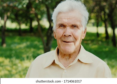 Portrait Of Happy Old Senior Man With Gray Hair Looking With Smile At Camera. Outdoors In Green Park. Elderly Aged People Care. 80 Years Old.