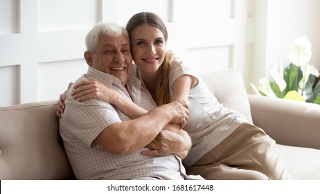 Portrait Happy Older Father And Adult Daughter Hugging, Looking At Camera, Posing For Photo, Beautiful Young Woman With Smiling Mature Dad Or Grandfather Sitting On Cozy Sofa At Home, Two Generations