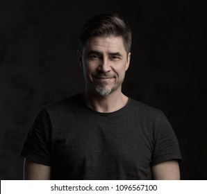 Portrait Of Happy Older Man In Casual Tshirt Smiling Isolated On Dark Background.