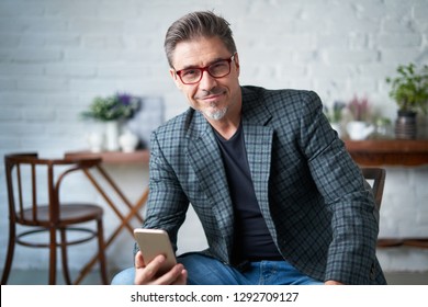 Portrait Of Happy Older White Man With Gray Hair Wearing Jacket Smiling Using Smart Phone. 
 .