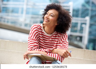 Portrait Of Happy Older Woman Sitting On Steps With Book And Pen