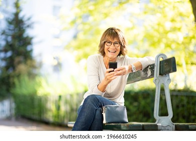 Portrait Happy Older Woman Sitting On Park Bench Using Cellphone