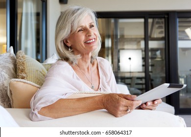 Portrait Of Happy Older Woman Sitting On Sofa With Digital Tablet