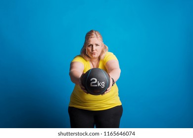 Portrait Of A Happy Overweight Woman Exercising With A Heavy Ball In Studio.