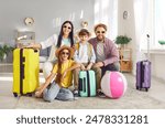 Portrait of happy parents with kids daughter and son sitting on the floor with packed suitcases and looking at camera ready to fly to tropical resort together. Family vacation and holiday trip.