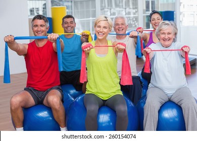 Portrait of happy people on fitness balls exercising with resistance bands in gym class - Powered by Shutterstock