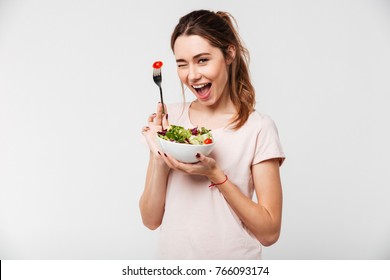 Portrait of a happy playful girl eating fresh salad from a bowl and winking isolated over white background - Shutterstock ID 766093174