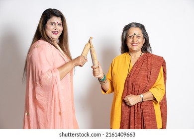 Portrait Of Happy Playful Mature Senior And Young Indian Woman Holding Rolling Pin And Wooden Spoon Isolated On White Background. Home Maker, Kitchen Concept.