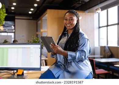 Portrait of happy plus size african american casual businesswoman using tablet in office. Casual office, business, lifestyle, communication and work, unaltered. - Powered by Shutterstock