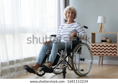 Portrait of happy positive handicapped old woman sitting in wheelchair feel optimistic at home or retirement house, smiling senior disabled female in invalid carriage wheel chair look at camera