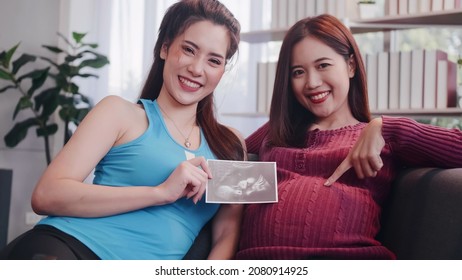 Portrait Of Happy Pregnant Lesbian Couple Sitting On Sofa At Home.