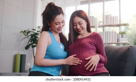 Portrait Of Happy Pregnant Lesbian Couple Sitting On Sofa At Home.