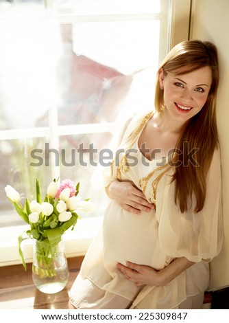 Portrait Of Happy Pregnant Woman Sitting Near Window