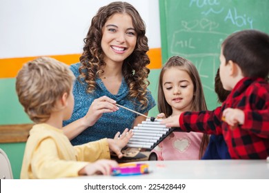 Portrait of happy preschool teacher and children playing with xylophone in classroom
