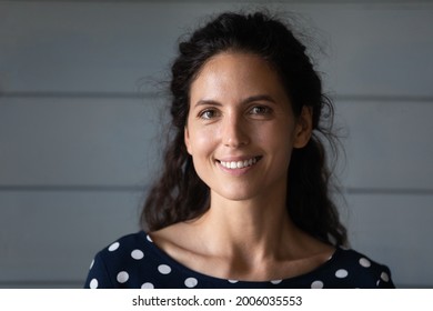 Portrait of happy pretty Hispanic 30s woman with black wavy hair looking at camera. Beautiful female model with toothy smile posing against grey background. Head shot, profile picture