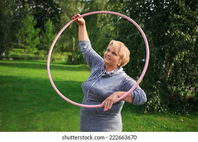 Portrait Of Happy Pretty Senior Woman Exercising With Colorful Hula Hoop On Nature Background