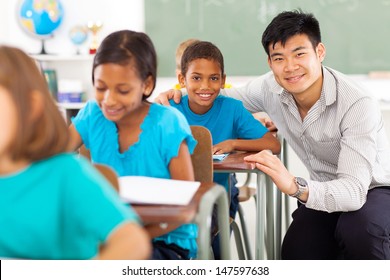 Portrait Of Happy Primary Teacher Helping Student In Classroom