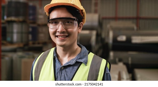 Portrait Of Happy Professional Asian Man Worker Wearing Safety Goggles And Helmet Standing Smiling And Looking At Camera In The Factory. Close Up Of Handsome Young Male Industry Engineer In Warehouse.