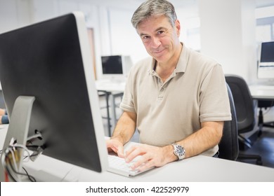 Retrato de un profesor feliz trabajando en una computadora en un aula