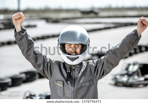 Portrait of a happy racer in\
protective sportswear standing as a winner of a go-kart race\
outdoors