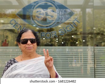 Portrait Of A Happy Retired Indian Woman Wearing UV-protecting Black Sunglasses For Physical Protection Of Eye Immediately After Surgery. Showing A Victory Sign - Defeat Cataract 
Delhi, India:2020