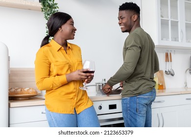 Portrait Of Happy Romantic Black Couple Spending Time In Kitchen Together, Cheerful Young African American Wife Drinking Red Wine While Her Husband Cooking Lunch On A Stove, Closeup Shot