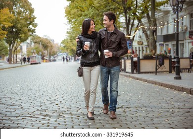 Portrait of a happy romantic couple with coffee walking outdoors in old european city