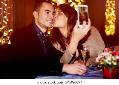 Portrait of a happy romantic couple making selfie photo with smart phone, cheerful girlfriend kissing her boyfriend on the cheek while taking self portrait - Powered by Shutterstock