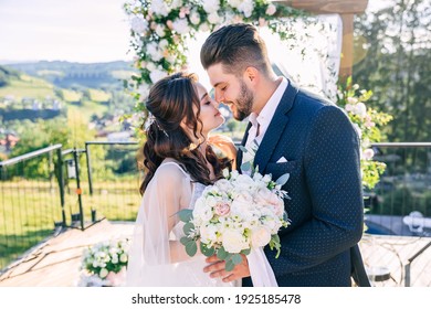 portrait of a happy, romantic newlywed couple kissing near an arch in the open air.