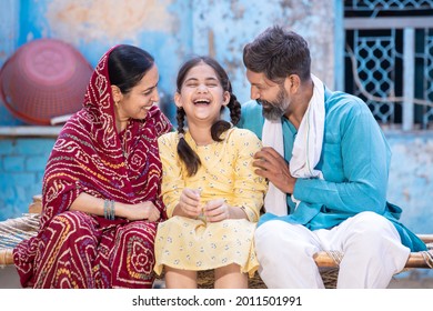 Portrait Of Happy Rural Indian Family Laughing And Having A Good Time Together While Sitting Outside At Village House, Cheerful Little Daughter Enjoy With Her Father And Mother. Parent With Child