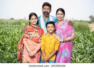 Portrait of happy rural indian family standing in agriculture field. Parents with their children, farmer husband wife with daughter and son. Beard man wearing kurta and woman wearing sari, 