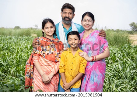 Portrait of happy rural indian family standing in agriculture field. Parents with their children, farmer husband wife with daughter and son. Beard man wearing kurta and woman wearing sari, 