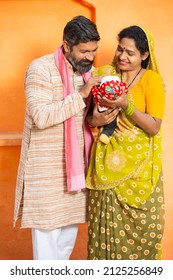 Portrait Of Happy Rural Indian Parents With Newborn Baby, Couple Father Mother Holding New Born Baby Against Orange Background.