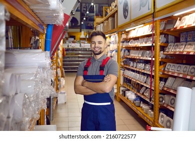 Portrait Of Happy Sales Assistant At Modern DIY Store Or Hardware Department At Shopping Centre. Handsome Young Man In Workwear Uniform Standing In Air Vent Pipes Aisle, Looking At Camera And Smiling