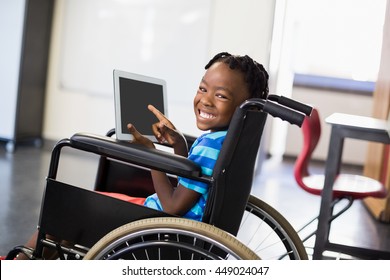 Portrait of happy schoolboy sitting on wheelchair and using digital tablet at school - Powered by Shutterstock