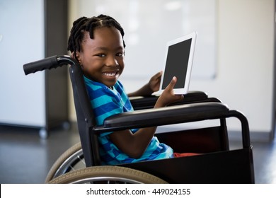 Portrait of happy schoolboy sitting on wheelchair and using digital tablet at school - Powered by Shutterstock