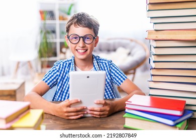 Portrait of a happy schoolboy with a tablet computer. A boy child sits at a table with stacks of books, and plays a game, uses a digital tablet for online lessons and information retrieval. - Powered by Shutterstock