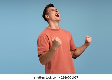 Portrait of happy screaming handsome young man standing with suprised face and rejoicing his victory. Indoor studio shot, isolated on blue background  - Shutterstock ID 2246701087