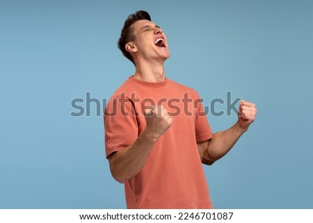 Portrait of happy screaming handsome young man standing with suprised face and rejoicing his victory. Indoor studio shot, isolated on blue background 